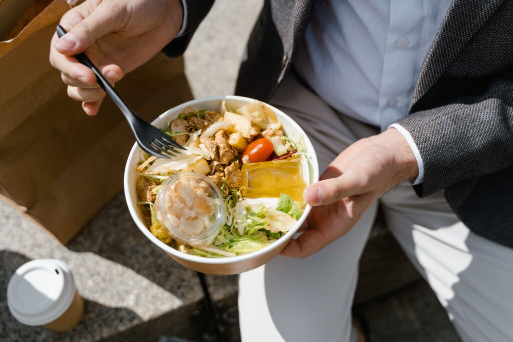 Man enjoying a fresh salad and coffee outdoors during lunch break in daylight.